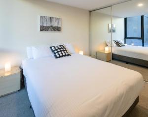a bedroom with a large white bed and a mirror at Melbourne City Apartments - Teri in Melbourne