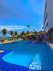 uma grande piscina azul com palmeiras e guarda-sóis em Tabatinga Flat - Beira Mar em Conde