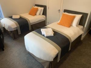 two beds in a room with orange and white pillows at Muir Bank in Muir of Ord