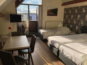 Cette chambre comprend deux lits, une table et une fenêtre. dans l'établissement Hotel Faber, à Zandvoort