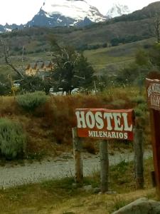 una señal en medio de un campo con una montaña en Milenarios Hostel en El Chalten