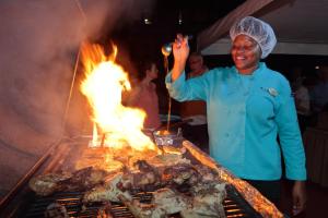 a woman standing in front of a grill with meat at Coconut Court Beach Hotel in Bridgetown