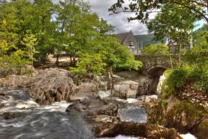 a river with a bridge and a house in the background at Semi Detached Cottage Snowdonia with hot tub in Tal-y-Cafn