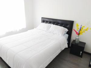 ein weißes Bett mit schwarzem Kopfteil und eine Vase mit Blumen in der Unterkunft 3 Apartamento completo Cedritos Minimalista in Bogotá
