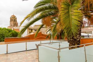 a balcony with a palm tree and a clock tower at Hospedium Hotel El Nido de Alcudia Suites in Almodóvar del Campo