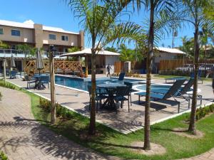 una piscina con mesa, sillas y palmeras en Village Praia do Surf, Itacimirim - Camaçari, BA en Itacimirim
