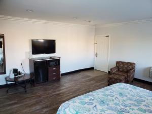 1 dormitorio con 1 cama, TV y silla en Ocean Surf Inn & Suites, en Huntington Beach