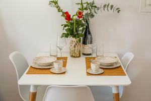 a white table with plates and glasses and a vase with flowers at La FLEUR apartments in Skiathos