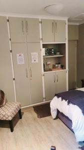 ein Schlafzimmer mit weißen Schränken, einem Bett und einem Stuhl in der Unterkunft THE SPARE BEDROOM Unit 1 in Harrismith