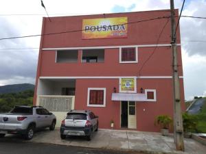 a red building with two cars parked in front of it at Pousada Sol de Minas in Monte Sião