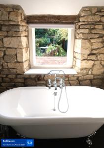 uma banheira em frente a uma parede de pedra com uma janela em Boutique cottage in the heart of Winchcombe em Winchcombe