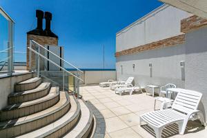 um pátio com cadeiras brancas e escadas num edifício em Ao lado da praia | Piscina vista MAR #IA06 em Florianópolis