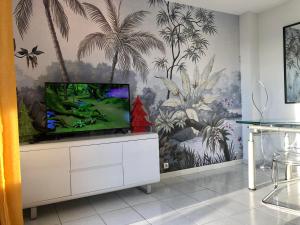een tv op een kast in een kamer met een muurschildering van palmbomen bij Barcaresa-VILLA SUR LE SABLE VUE MER PANORAMIQUE PISCINE CLIM WIFI in Le Barcarès