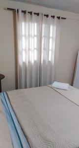 a bedroom with a bed and a window with white curtains at Hospedagem Doce Lar - Casa Girassol in Teresópolis