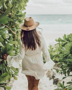 a woman in a hat walking on the beach at NEST Tulum in Tulum