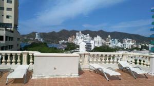 a group of white benches on a balcony with a city at Aparta Hotel Roca Marina in Santa Marta