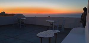 Aethrio Sunset Village - Oia في أويا: إطلالة على غروب الشمس من شرفة مع طاولات وكراسي