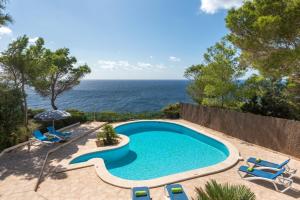 una piscina con sillas, una sombrilla y el océano en Villa Llevant Galdana, en Cala Galdana