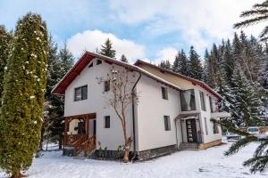 une maison blanche dans la neige avec des arbres dans l'établissement Casa Danielle, à Topliţa