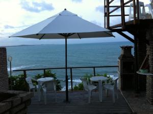 a patio with an umbrella and chairs and the ocean at Pousada Farol Eco Adventure in Baía Formosa