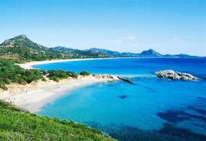 uma praia com água azul e montanhas ao fundo em B&B Nel Giardino In Fiore em Castiadas