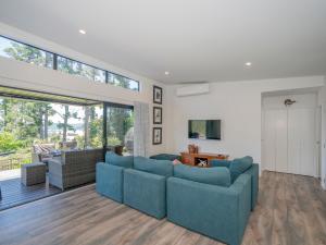 - un salon avec des canapés bleus et une grande fenêtre dans l'établissement Treetop Bach - Whangamata Holiday Home, à Whangamata