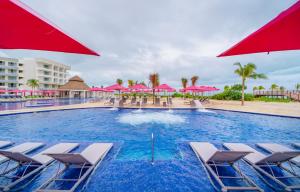 a large swimming pool with chairs and pink umbrellas at Planet Hollywood Cancun, An Autograph Collection All-Inclusive Resort in Cancún