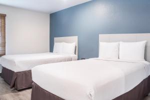 two white beds in a room with blue walls at WoodSpring Suites McKinney in McKinney