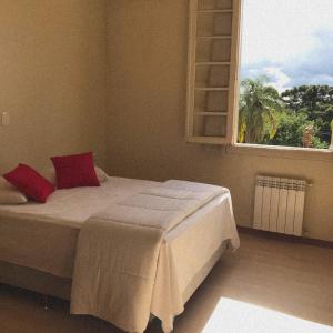 a bedroom with a bed with red pillows and a window at Hotel Murialdo in Caxias do Sul