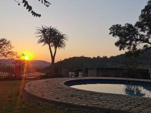 een zwembad in een tuin met een zonsondergang op de achtergrond bij MacNut Bed and Breakfast in Nelspruit
