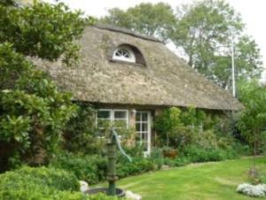 ein Haus mit einem Strohdach und einem Garten in der Unterkunft Little Rose Cottage in Börm