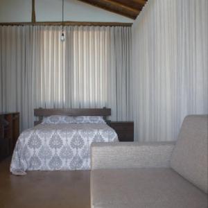 een slaapkamer met een bed met gordijnen en een bank bij Chalés Beija-flor in Itambé do Mato Dentro