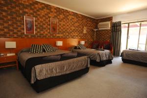 a bedroom with three beds and a brick wall at Horsham Mid City Court Motel in Horsham