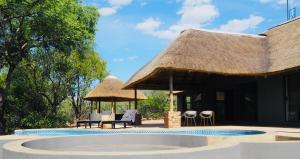 a pool with a thatched roof and chairs and tables at Pata Pata House in Marloth Park