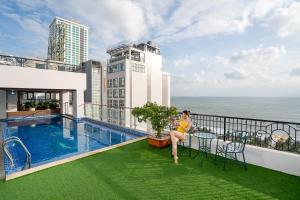 a woman sitting on the balcony of a building with a swimming pool at Apus Hotel in Nha Trang