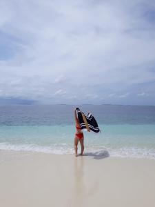 a person standing on a beach holding a surfboard at Island Break in Fulidhoo