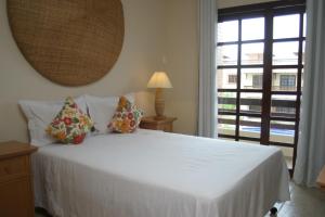 a bedroom with a white bed with pillows and a window at CostaSol Pipa Chalés in Pipa