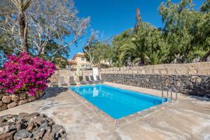 a swimming pool with a stone wall and purple flowers at La Casita in Adeje