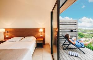 a woman sitting in a chair reading a book on a balcony at Résidence Les Terrasses de Rondinara in Bonifacio