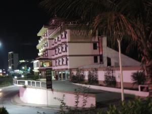 un edificio rosa y blanco por la noche con una palmera en Hotel Beira Rio, en Brusque