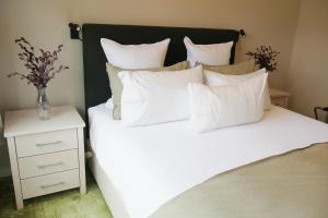 un letto con cuscini bianchi e un vaso su un comodino di Apartment on St Georges a Havelock North