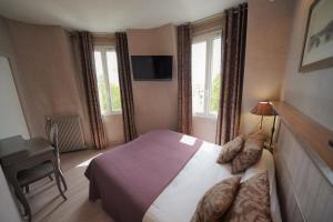 a bedroom with a bed and a desk and windows at Hôtel du Château in Vincennes