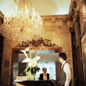 Ein Mann steht vor einem Tisch mit einem Kronleuchter. in der Unterkunft Hotel Ambassador in Wien