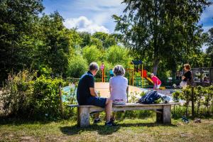 a man and woman sitting on a bench in front of a playground at Welcome in - Oranjezon - Vakantiehuis 6 personen in Vrouwenpolder