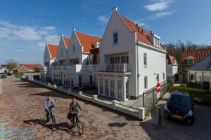 two people riding bikes in front of a row of houses at Appartement - Kaapduinseweg 13 Dishoek 13A Luxe 4 personen in Dishoek