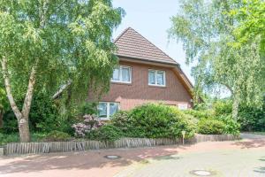 ein rotes Backsteinhaus mit einem Zaun und Bäumen in der Unterkunft Landhaus Braband Ferienwohnungen - Gustav-Schönleber-Weg 2 in Cuxhaven