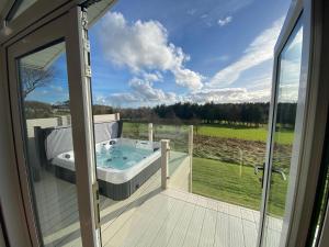uma banheira de hidromassagem num deque com uma porta de vidro em Hot Tub Lodge with Panoramic Views & Free Golf em Swarland