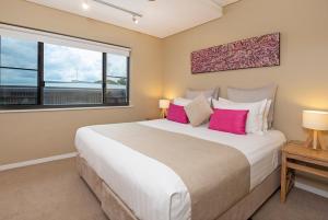 a bedroom with a large bed with pink pillows at Saltwater Suites - 1,2 & 3 Bed Waterfront Apartments in Darwin