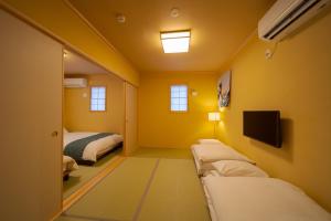 a yellow room with two beds and a tv at Yufuin Matsuri-an Nagomiya in Yufuin