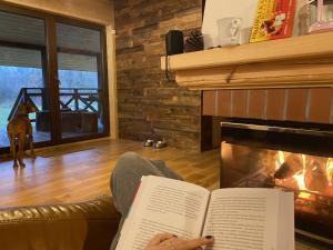a person reading a book in front of a fireplace at Dom w krainie Bugu in Korczew
